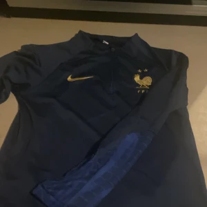 Frankrike fotbollströja långärmad - Mörkblå långärmad fotbollströja från Nike med Frankrikes landslagslogga och två guldstjärnor på bröstet. Guldigt Nike-märke på ena sidan. 