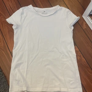 Vit t-shirt från H&M - En klassisk vit t-shirt från H&M i mjuk bomull. T-shirten har rund halsringning och korta ärmar, perfekt för en enkel och stilren look. Passar till det mesta och är ett måste i garderoben.