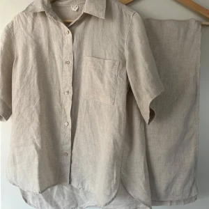 ARKET Linne set - Ett matchande set bestående av en kortärmad skjorta och ett par vida byxor. Skjortan har en klassisk krage, knäppning framtill och en bröstficka. Byxorna har resår i midjan med dragsko. Byxorna har fickor i sidan.   Skjortan är en äldre modell av denna:   https://www.arket.com/sv-se/product/relaxed-linen-shirt-beige-1262613001/  Skillnaden är fickan vid bröstet.   Byxorna är dessa:   https://www.arket.com/sv-se/product/linen-drawstring-trousers-beige-1068990002/  De har använts 2-3 gånger och är