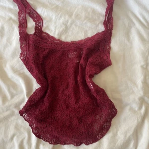 Vinröd spetslinne - Vinrött linne i spets från Urban Outfitters. Linnet är ärmlöst och har tunna axelband, helt i genombruten spets med blommigt mönster. Perfekt att styla lager på lager eller som statement-piece.