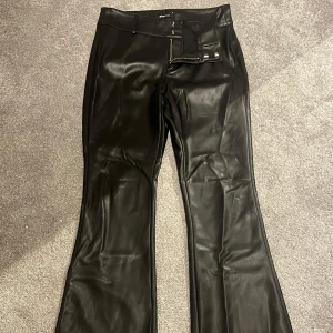 Svarta skinnbyxor från Gina Tricot - Säljer ett par svarta skinnbyxor från Gina Tricot med normal passform och bootcut-stil. Byxorna har dragkedja och knapp framtill samt hällor för bälte. Snygga och trendiga byxor som passar till många olika outfits. pris kan diskuteras!!