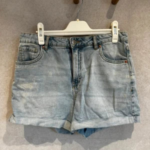 Ljusblå jeansshorts 170 - Säljer ett par ljusblå jeansshorts med klassisk femficksdesign och upprullad kant nedtill. Shortsen har normal passform och stängs med knapp och dragkedja. Perfekta för varma dagar! Märket är LAB från Kappahl