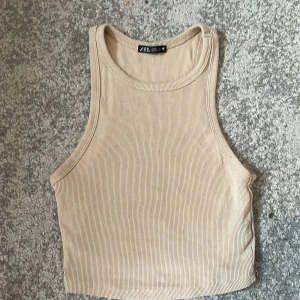 Beige ribbad croppad linnetopp från Zara - Säljer en beige croppad linnetopp från Zara. Toppen är ribbad och har en ärmlös design med rund halsringning. Perfekt för varma dagar och enkel att matcha med olika outfits.