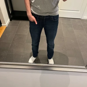 Mörkblå slim fit jeans från Jack & Jones - Säljer ett par mörkblå slim fit jeans från Jack & Jones. Klassisk femficksmodell med dragkedja och knapp i midjan. Jeansen har en snygg tvätt och smal passform som sitter tajt längs benen. Perfekta för en stilren look. Storlek 30/30