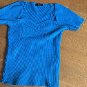 Blå ribbad topp med sweetheart-urringning - Säljer en blå ribbad topp med korta ärmar och snygg sweetheart-urringning. Toppen har en figurnära passform och är tillverkad i ett stretchigt material som sitter bekvämt. Perfekt att styla till jeans eller kjol!