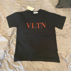 Svart t-shirt från Valentino med röd VLTN-logga - Säljer en svart t-shirt från Valentino med röd VLTN-logga på bröstet. Tröjan är köpt från vestiarie. Skriv vid funderingar. Passar nån som är 167-175. 
