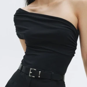 Svart oneshoulder body - Säljer en svart body med oneshoulder-design och draperad överdel. Sitter tight och har en elegant, asymmetrisk skärning som ger en stilren look. Helt ny, aldrig använd 