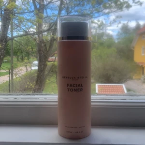 Rebecca Stella Facial Toner - En ansiktstoner från Rebecca Stella i en stilren, ljusrosa flaska med gulddetaljer. Produkten är på 200 ml och helt ny.