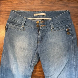 Blå jeans - Snygga blå jeansbyxor med dekorativa knappar framtill och vid fickorna. normal passform och vida ben. Perfekta till vardags och lätta att matcha med olika toppar.