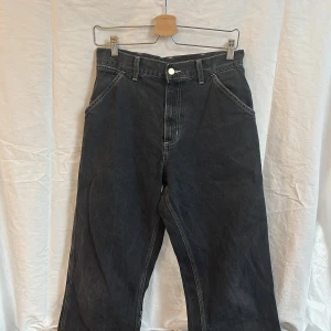 Svarta jeans Carhartt simple pant 28/32 - Säljer ett par svarta jeans från Carhartt. Liten reva på ena benet. Se bild. 