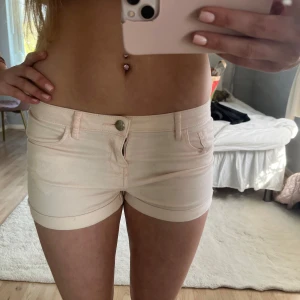 Lågmidjade ljusrosa jeansshorts - Säljer ett par supersöta lågmidjade rosa jeansshorts!  Shortsen har bälteshällor och stängs med knapp och dragkedja. Perfekta för varma dagar och enkla att matcha med olika toppar.