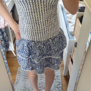 Vit och blå volangklänning från Gina Tricot - Supersöt kortklänning från Gina Tricot i vitt och blått med smockad överdel och volangkjol. Klänningen är ärmlös och har ett lekfullt mönster samt volangdetaljer nertill. Perfekt för varma dagar!Har användit några gånger men i nyskick.  Frakt ingår inte. Säljer för att jag har växt ur dem. 