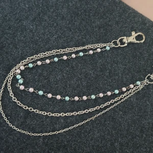 Silverfärgad kedja med pärlor - Säljer en snygg silverfärgad kedja med två lager kedjor och ett lager med små pärlor i ljusrosa och ljusblått. Kedjan har karbinhakar i båda ändar och passar perfekt som accessoar till exempelvis glasögon eller byxor.