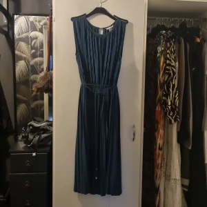 Petrolfärrgad långklänning med plisserad design - Säljer en elegant petrolfärgad långklänning med plisserad överdel och kjol. Klänningen har ett smalt band i midjan och är ärmlös, vilket ger en stilren och tidlös look. Perfekt för speciella tillfällen när du vill känna dig extra fin. Pris:500kr