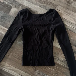 Svart långärmad topp från Gina Tricot - Säljer en svart långärmad topp från Gina Tricot i ribbat material. Toppen har en djupare rundad ringning bak. Alltså lite öppen rygg! 