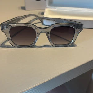 Grå transparenta solglasögon från CHIMI - Snygga solglasögon från CHIMI med transparent grå båge och mörka glas. Rektangulär form med tjockare bågar som ger en modern look. Perfekta för dig som vill sticka ut med stilrena accessoarer.