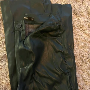 Mörkgröna skinnbyxor från Bik Bok - Säljer ett par mörkgröna skinnbyxor från Bik Bok. Byxorna har hög midja och raka ben