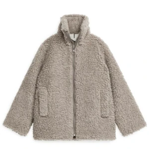 Arket teddyjacka med dragkedja  - Mysig beige teddyjacka från Arket med hög krage och dragkedja framtill. 58% ull och 42% polyester. Jackan har två stora fickor på sidorna och är helfodrad. Jackan är perfekt för kyliga dagar och ger en trendig look med sin fluffiga struktur.