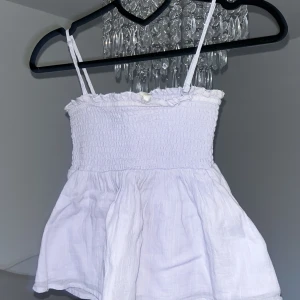 Ginatricot Young Ljuslila linnetopp  - Söt ljuslila linnetopp med smockad överdel och tunna axelband. Toppen har volangkant upptill och är lätt utsvängd nertill. Stretchig.