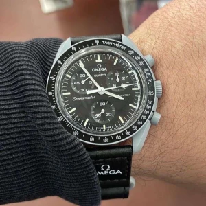 Omega x Swatch Speedmaster klocka - Snygg svart Omega x Swatch Speedmaster med svart urtavla och tachymeter-bezel. Klockan har tydliga vita markeringar och visare samt svart textilband med Omega-logga. Perfekt accessoar för dig som gillar klassisk och sportig stil.
