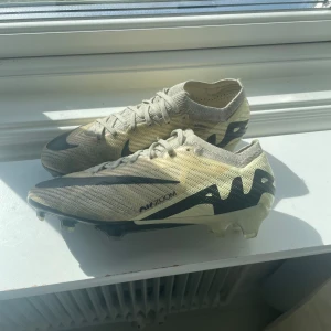 Nike Mercurial vapor 15 elite i beige och svart - Säljer ett par Nike  Mercurial vapor 15 fotbollsskor i beige med svarta detaljer och snörning. Perfekta för dig som vill ha lätta och snabba skor på fotbollsplanen. Påsen och boxen kommer med och påsen har en fläck och en reva i sig.