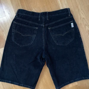 Svarta manchester shorts, Guess Jeans - Svarta shorts i manchester från Guess Jeans. Shortsens material ger en cool retrovibe och de har en normal passform, lite jorts-aktiga🩷