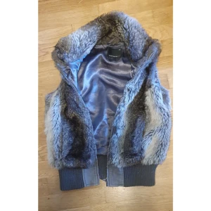 Grå/brun pälsväst med ribbad kant - Snygg y2k grå pälsväst med mjukt foder och bred ribbad kant nedtill. Västen har en klassisk krage och är perfekt för lager-på-lager-stil. Passar till många olika outfits och håller dig varm under kyliga dagar.