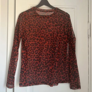 Röd meshtopp med leopardmönster - Tunn, röd meshtröja med svart leopardmönster. Vet ej märke eftersom den är köpt second hand. Så snygg under tex en väst eller klänning!