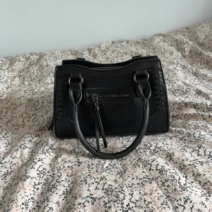 Svart handväska med detaljer - Säljer en sååå fin svart handväska med två handtag och dekorativa sömmar på sidorna. Perfekt storlek för det viktigaste och enkel att matcha till olika outfits. Endast använd 2 gånger, så är som ny utan defekter! Tveka inte att höra av dig💓💕Höjd: ca 14 cm, bred: ca 20cm💕