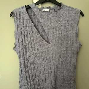 topp från Zara - Säljer en grå/lila croppad topp från Zara cut out. Toppen är ärmlös och har en ribbad struktur i materialet. Perfekt för dig som gillar unika snitt och trendiga detaljer. 