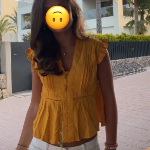 Gul blus med volang från LDN - Säljer en solgul blus från LDN med v-ringning, knappar framtill och volangdetaljer vid axlarna. Blusen är i storlek xs och använd 2 gånger