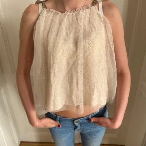 Beige glittrig linnetopp med rosettband - Säljer en söt beige linnetopp med glittrigt tyg och tunna axelband som knyts i rosetter. Ingen lapp men skulle säga storlek XS!