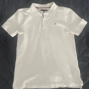 Vit piké från Tommy Hilfiger - Klassisk vit piké t-shirt från Tommy Hilfiger med liten broderad logga på bröstet. Den har används men inga stora defekter. Strl 52, vilket motsvarar ungefär XS. Hör gärna av om du undrar något!