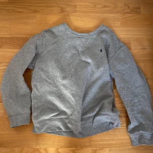 Grå sweatshirt från Polo Ralph Lauren - Säljer en klassisk grå sweatshirt från Polo Ralph Lauren med broderad logga på bröstet. Tröjan har rund halsringning och långa ärmar. Perfekt för en avslappnad och stilren look.