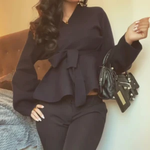 Svart kavaj/tröja med rosett och vida ärmar - Säljer en svart blus med markerad midja och stor rosett framtill. Blusen har vida, långa ärmar och en lätt v-ringning. Perfekt för dig som gillar stilrena och feminina detaljer.