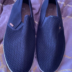Svarta slip-on sneakers med mesh - Säljer ett par svarta slip-on sneakers med ovandel i mesh och detaljer i beige. 