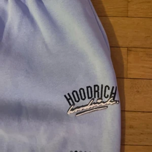 Ljuslila mjukisbyxor från Hoodrich - Säljer ett par ljuslila mjukisbyxor från Hoodrich med broderad logga på ena benet. Byxorna har resår i midjan med snörning och muddar vid bensluten. Perfekta för en avslappnad stil.