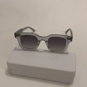 Äkta grå transparenta solglasögon från CHIMI - Snygga solglasögon från CHIMI med transparent grå båge och fyrkantig form. Glasen är mörktonade och ger en cool look. Perfekt accessoar för soliga dagar.