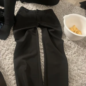 Svarta kostymbyxor från Gina Tricot - Säljer ett par klassiska svarta kostymbyxor från Gina Tricot. Byxorna har rak passform och normal midja, perfekta för en stilren look. Passar till många olika outfits och är ett måste i garderoben.