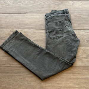 Grå jeansbyxor från Replay - Säljer ett par grå jeansbyxor från Replay, modell Thad. Byxorna har klassisk femficksdesign, raka ben och normal passform. Snygga detaljer med Replay-logga vid fickan och diskret broderi på bakfickan.
