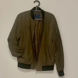 Mörkt olivgrön bomberjacka Zara man strl L - En supersnygg bomberjacka från Zara man men jag tycker jackor är unisex för det mesta. Det är iaf jag som använt den 👍🏻 Den går i en mörkare olivgrön ton med svarta muddar vid är slut och kragen. Det finns 2 innerfickor. Mycket gott skick. Katter finns i hemmet .