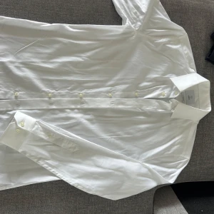 Vit skjorta från Bläck - Klassisk vit skjorta från Black i modellen Tailored Fit. Skjortan har lång ärm, knappar framtill och vid manschetten. Perfekt för en stilren look och passar till många olika tillfällen.