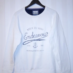 Vit sweatshirt från Race Marine L - Vit sweatshirt från Race Marine med tryck 'Endeavour' och marin ankardetalj på bröstet. Tröjan har rund hals, långa ärmar och är gjord i mjuk bomull och polyester. Perfekt för en chill och sportig look med skandinavisk känsla. Kan skickas med extra pris via post.