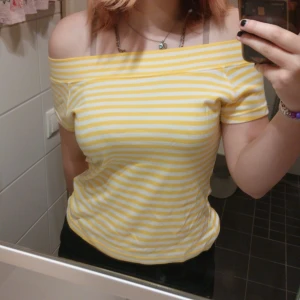 Gulvit offshoulder topp - Superfin gul och vit randig topp från Trend.DK med offshoulder-modell. Toppen har korta ärmar och sitter snyggt med en normal passform. Fick i födelsedagspresent och endast använt 2 gånger.