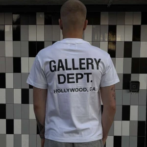 Vit t-shirt från Gallery Dept. - Vit t-shirt från Gallery Dept. med svart tryck både fram och bak. Klassisk passform med rund hals och korta ärmar. Stort tryck på ryggen med texten 'GALLERY DEPT. HOLLYWOOD, CA.' och mindre logga på bröstet. Perfekt basic med streetkänsla.
