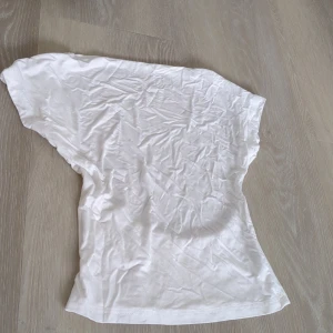 Vit topp med öppen rygg - Säljer en vit topp med korta ärmar och snyggt öppen rygg. Modellen är loose och har en enkel, stilren look. Tillverkad i mjuk viskosblandning med stretch för extra komfort. Perfekt för dig som gillar minimalistisk stil och vill ha något luftigt.