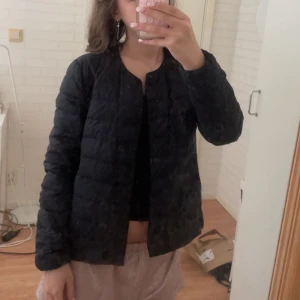 Svart uniqlo jacka - Säljer en svart, quiltad dunjacka med rund halsringning och knäppning framtill. 