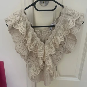 Beige stickad topp med spetsvolanger - Supersöt beige stickad topp från Zara med breda volanger i spets längs axlar och ringning. Toppen säljs inte längre av Zara och är i storlek S. Säljer pågrund av att jag inte har använt den på senaste💓 