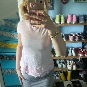 Ljusrosa T-shirt - Supersöt ljusrosa tröja med korta ärmar och vacker spetskant nertill. Tröjan har broderad logga framtill och är gjord i mjuk bomull. Perfekt för dig som gillar romantiska detaljer och en feminin look.