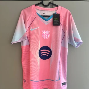 Barça Lamine Yamal rosa matchtröja Nike - Snygg FC Barcelona fotbollströja i rosa och ljusblått med Lamine Yamal 19 på ryggen. Tröjan har korta ärmar, Nike-logga, FCB-emblem och Spotify-logga på bröstet. Tillverkad i lätt och ventilerande material, perfekt för fotbollsplanen eller att bära som supporter.